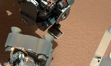The Curiosity Rover uses it's robotic arm to scoop sand.