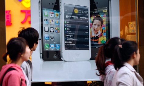 Chinese walk in front of an iPhone poster at a phone shop in Beijing Saturday, April 7, 2012. 