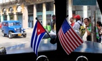 A car drives through Havana, Cuba with American and Cuban flags on its dashboard.