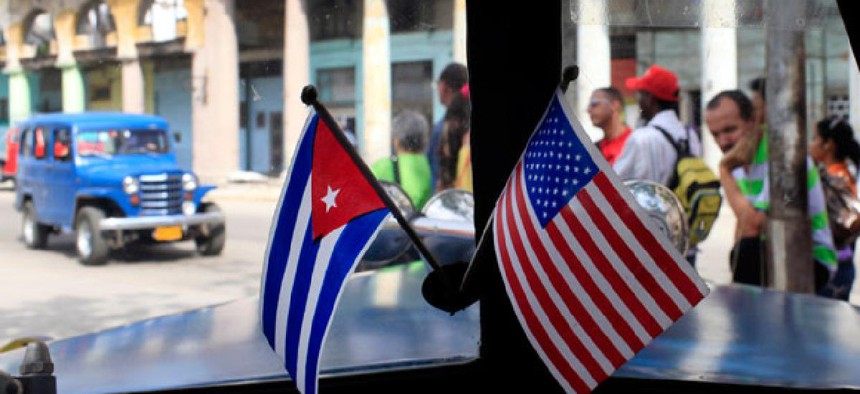A car drives through Havana, Cuba with American and Cuban flags on its dashboard.