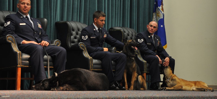 Handlers SSgt. Dwight Veon, SSgt. Jesse Galvan, and SSgt. James Cochran sat next to their dogs Blacky, Cita, and Sheila during a retirement ceremony held at Tinker Air Force Base on June 25.