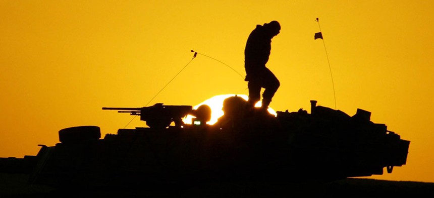  U.S. soldier walks atop his armored vehicle at sunset as he prepares for a nighttime military exercise in the Kuwaiti desert.