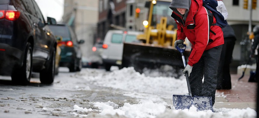 Workers clear newly-fallen snow from a street, Tuesday, Feb. 18, 2014, in Trenton, N.J.