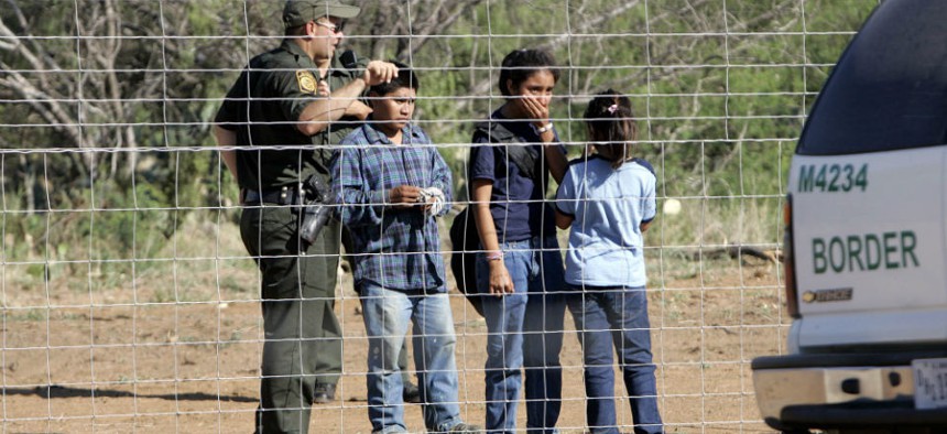 A Border Patrol agent stands on a ranch fence line with children taken into custody in South Texas brush country north of Laredo, Texas.
