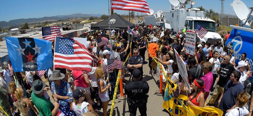 Demonstrators from opposing sides confront each other while being separated by Murrieta police officers, July 4, 2014, outside a U.S. Border Patrol station in Murrieta, Calif. 