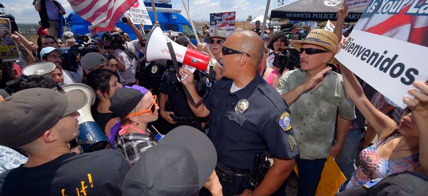 A Murrieta police sergeant talks to demonstrators as they confront each other, Friday, July 4, 2014, outside a U.S. Border Patrol station in Murrieta, Calif. 