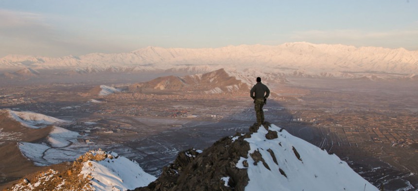 A coalition force member stands on top of a hill watching a snow-covered mountain range in Kabul province, Afghanistan.