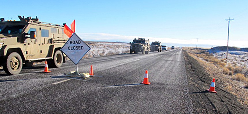 A convoy of armored vehicles and SUVs rolls past a barricade on the road near the Malheur National Wildlife Refuge on Jan. 30.