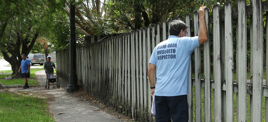 Giraldo Carratala, an inspector with the Miami- Dade County mosquito control unit, looks through a fence into the back yard of a home while doing a routine inspection earlier this month.