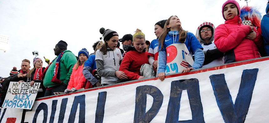 Fans stand behind a large sign for equal pay for the women's soccer team during an international friendly soccer match between the United States and Colombia in April.