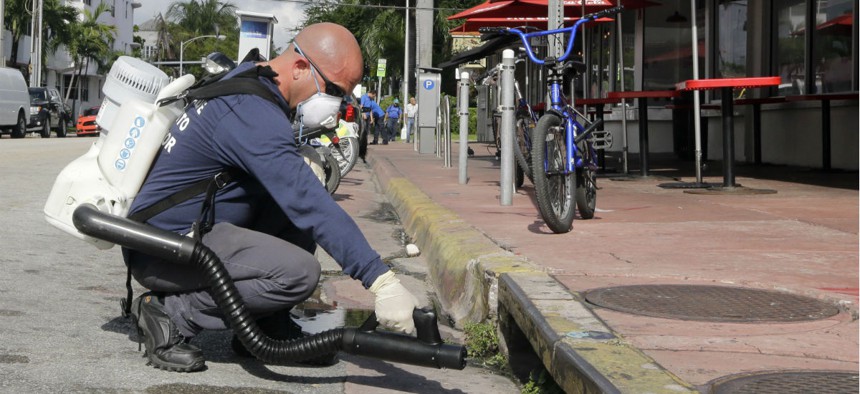 A Miami-Dade mosquito control inspector sprays a chemical mist into a storm drain.