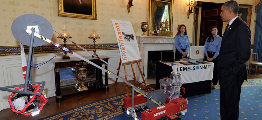 Barack Obama looks over a remotely operated vehicle to help firefighters with ice search and rescue calls developed by Olivia Van Amsterdam, left, and Katelyn Sweeney, center, at the White House Science Fair in 2014.