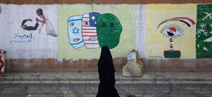 A woman walks past anti-Saudi and U.S. graffiti sprayed on a wall of the closed Saudi embassy in Sanaa, Yemen in 2015.