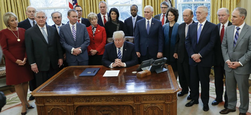 President Trump signs the reorganization executive order with members of his Cabinet looking on. 