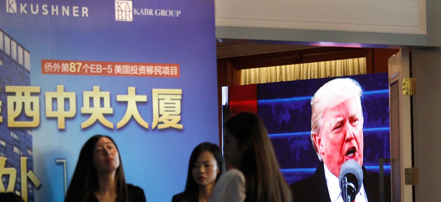  projector screen shows a footage of U.S. President Donald Trump as workers wait for investors at a reception desk during an event promoting EB-5 investment in a Kushner Companies development at a hotel in Shanghai, China, Sunday, May 7, 2017. 