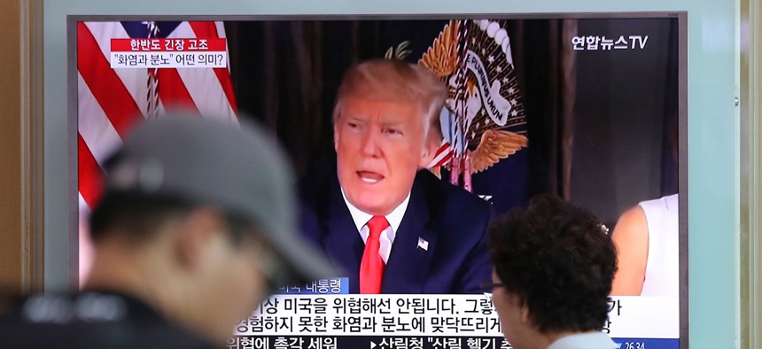 People walk by a TV screen showing a local news program reporting with an image of U.S. President Donald Trump at the Seoul Train Station Wednesday.