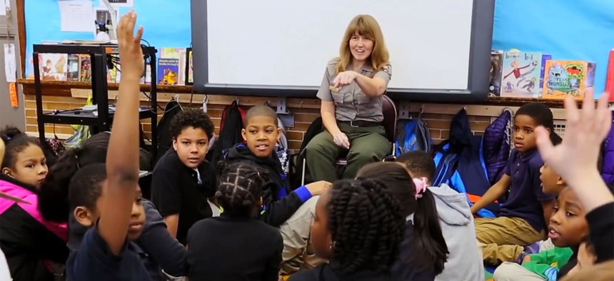 A screenshot from the ad shows a federal employee speaking to children.