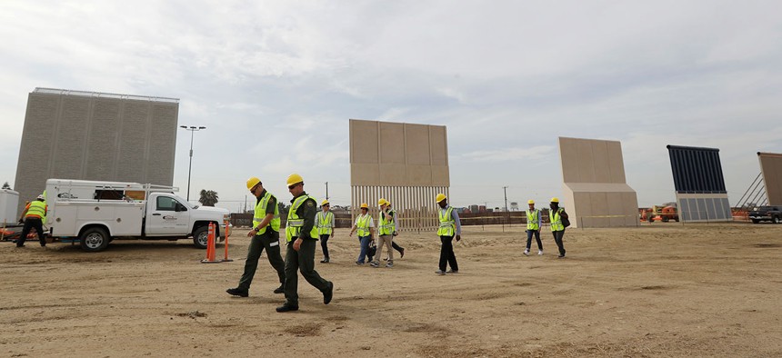 People pass border wall prototypes as they stand near San Diego on Oct. 19.