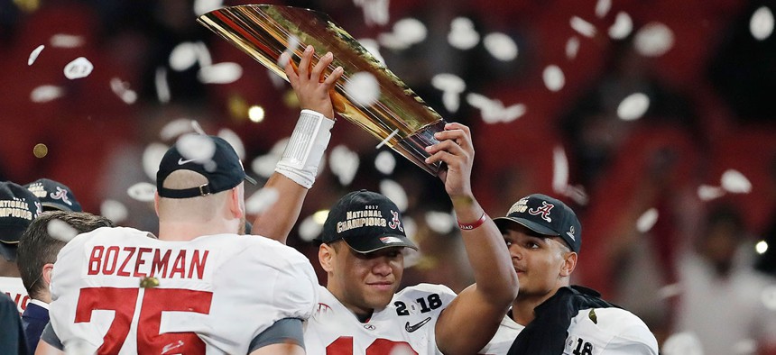 Alabama's Tua Tagovailoa holds up the national championship trophy after the team's victory.