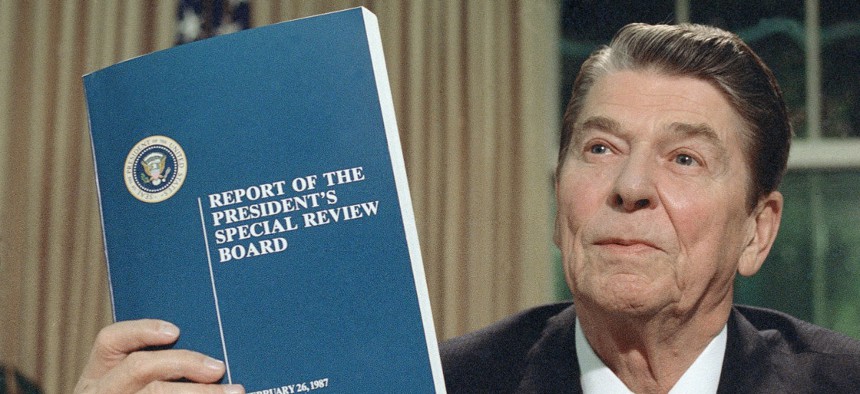 President Ronald Reagan holds up a copy of the Tower Commission report on the Iran-Contra affair, while posing for photographers after his nationally televised speech from the Oval Office on Aug. 13, 1987. 