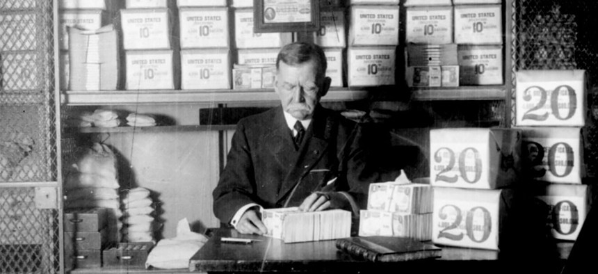 An unnamed Treasury Department official, surrounded by packages of newly minted currency, counting and wrapping dollar bills. Washington, DC 1907. 