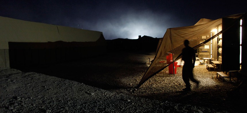A U.S. Marine exits a steel container, the lights illuminating the smoke from a trash-burning pit, at Forward Operating Base Jackson, in Sangin, Helmand province, Afghanistan in 2002.