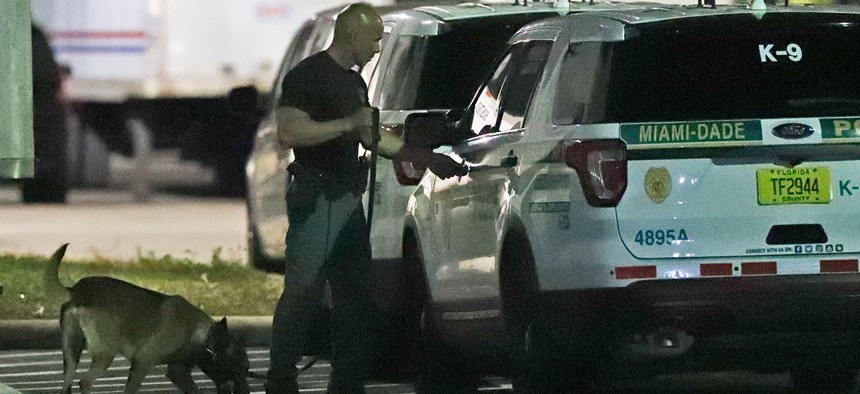 A police officer and dog are shown outside a postal facility on Thursday in Opa-locka, Fla. Investigators searched coast-to-coast Thursday for the culprit and motives behind the bizarre mail-bomb plot aimed at critics of the president. 