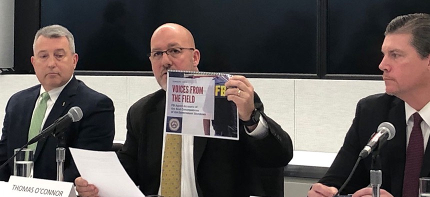 Thomas O’Connor (center), president of the FBI Agents Association, holds up a booklet with testimonials about the shutdown's impact. 