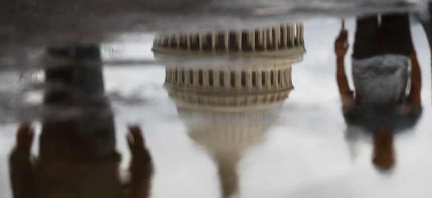 The Capitol Building and pedestrians are reflected in a puddle in 2017.