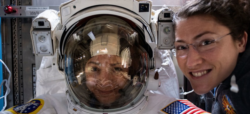 NASA astronaut Christina Koch (right) poses for a portrait with fellow Expedition 61 Flight Engineer Jessica Meir of NASA who is inside a U.S. spacesuit for a fit check.