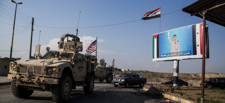 A U.S. military convoy drives through the town of Qamishli, north Syria, by a billboard showing Syrian President Bashar Assad on Saturday, Oct. 26. 2019.