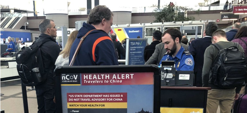 A health alert for people traveling to China is shown at a TSA security checkpoint at the Denver International Airport. Many federal employees and contractors face exposure to the novel coronavirus in the course of their work.
