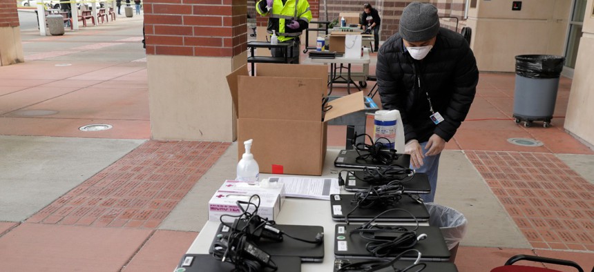 Minh Nguyen, a technology services worker with the Tacoma School District, cleans laptops that will be distributed to students for remote learning, Wednesday, April 1, 2020, in Tacoma, Wash. 