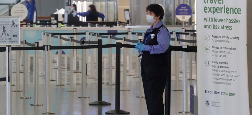 A worker wears a mask while standing near a TSA precheck entrance in a terminal at San Francisco International Airport. 