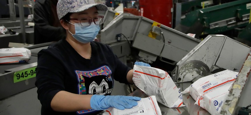 Postal workers wear masks and gloves as they sort mail at the U.S. Postal Service processing and distribution center on April 30 in Oakland, Calif. 