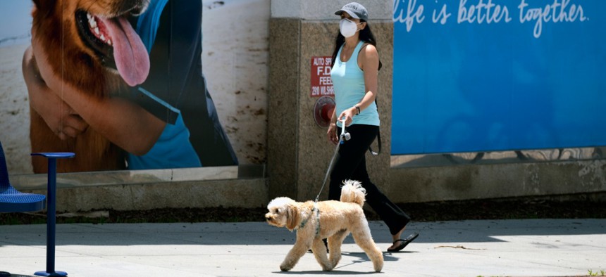 A woman wearing a protective mask for protection from the new coronavirus walks her dog in Santa Monica, Calif., on Saturday, May 9.