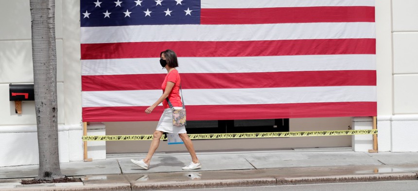 A woman wearing a protective face mask walks past an American flag in front of a closed business in Florida on Monday.