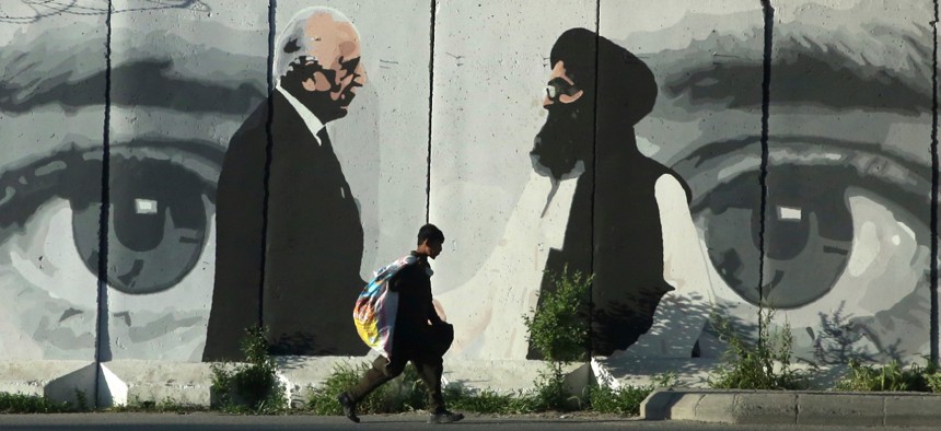 A young boy walks past a wall depicting Washington's peace envoy Zalmay Khalilzad, left, and Mullah Abdul Ghani Baradar, the leader of the Taliban delegation, in Kabul, Afghanistan, on May 5. 