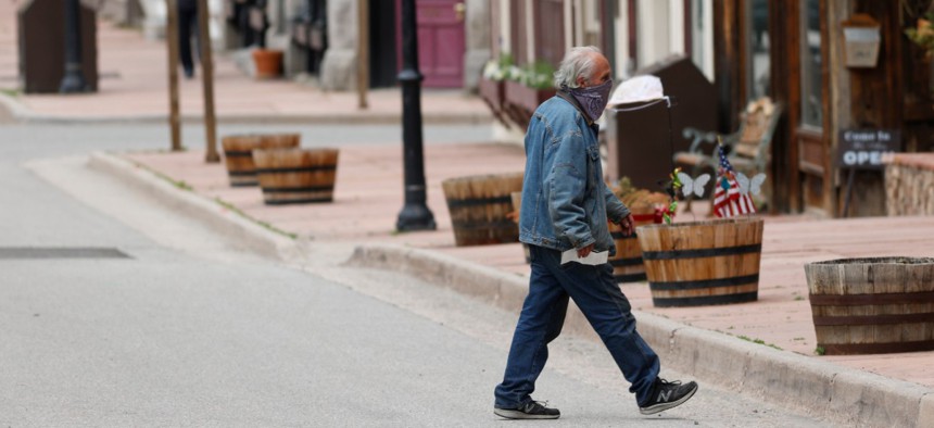 A pedestrian wears a face mask while crossing Sixth Street as businesses start to reopen, Wednesday, May 27, 2020, in Georgetown, Colorado. 