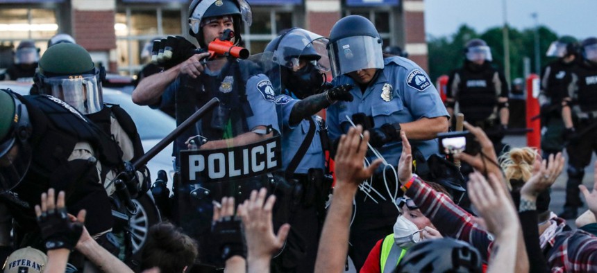 A police officer points a hand cannon at protesters who have been detained pending arrest on May 31 in Minneapolis. Protests following the death of George Floyd could result in a spike in coronavirus cases, health officials predict. 