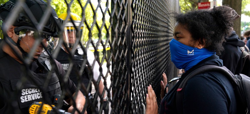A demonstrator watches as a U.S. Secret Service police office works on a fence blocking Lafayette Park as protests in the death of George Floyd continue on Tuesday, June 2, near the White House.