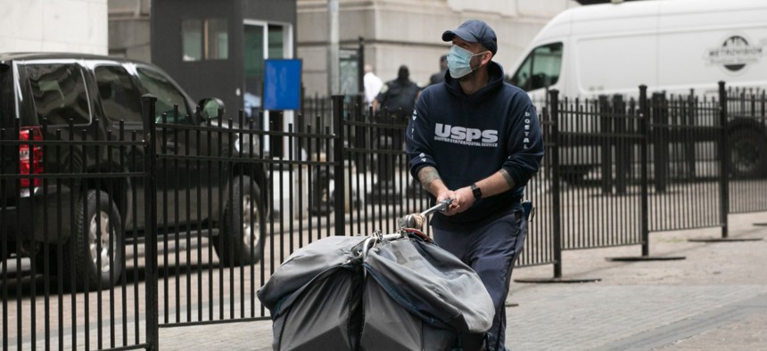 A masked postal worker pushes a cart of mail as he makes his rounds, Tuesday, May 26, 2020, in New York.