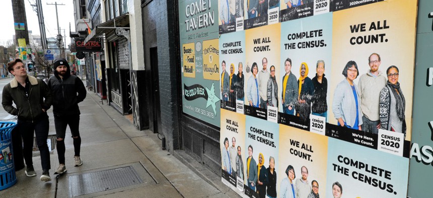 People walk past posters encouraging participation in the 2020 Census, Wednesday, April 1, 2020, in Seattle's Capitol Hill neighborhood. 