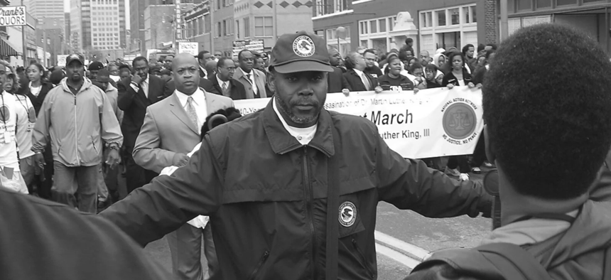 A staff member of the Community Relations Service mediating at a march in Memphis in 2009. His jacket and hat displayed the Department of Justice seal.