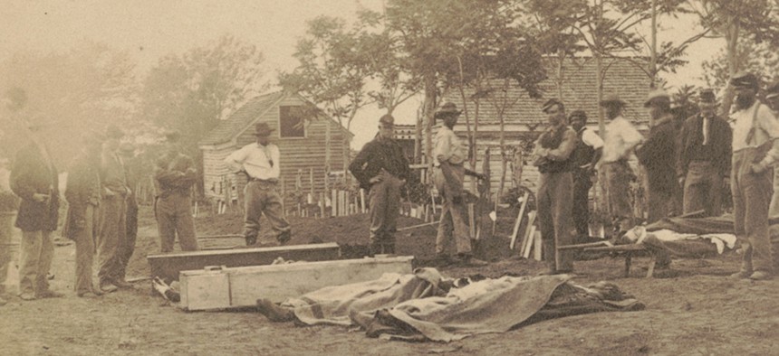 Soldiers and African American workers standing near caskets and dead bodies covered with cloths during Grant’s Overland Campaign.