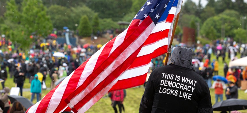  Man wearing a "This is what democracy looks like" shirt holds an American flag at a protest in Seattle in June.