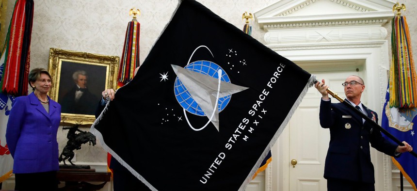 Secretary of the Air Force Barbara Barrett, left, watches Chief Master Sgt. Roger Towberman holds the United States Space Force flag as it is presented in the Oval Office of the White House, Friday, May 15, 2020.