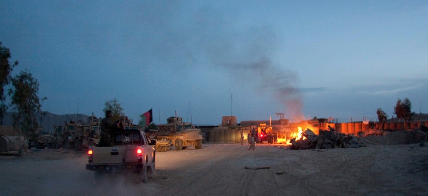 An Afghan National Army pickup truck passes parked U.S. armored military vehicles, as smoke rises from a fire in a trash burn pit at Forward Operating Base Caferetta Nawzad, Helmand province south of Kabu in 2011.