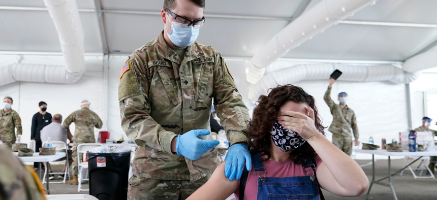 Leanne Montenegro, 21, covers her eyes as she doesn't like the sight of needles, while she receives the Pfizer COVID-19 vaccine at a FEMA vaccination center at Miami Dade College in Miami. 
