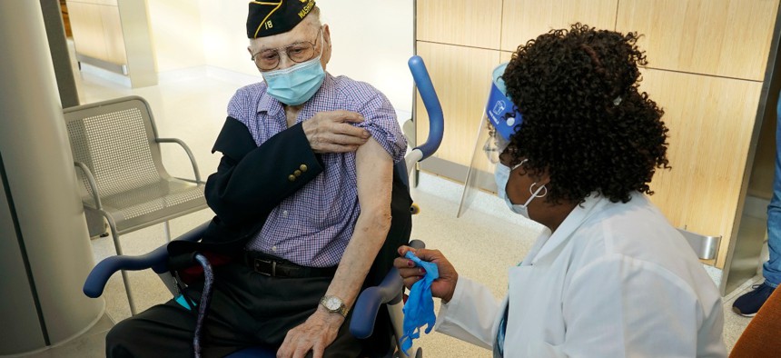 U.S. Army veteran Gene Moy, 103, left, of Seattle prepares to get the second shot of the Pfizer COVID-19 vaccination, Tuesday, Feb. 23, 2021, from Levone Walton, right, a nurse at the VA Puget Sound Health Care System campus in Seattle. 